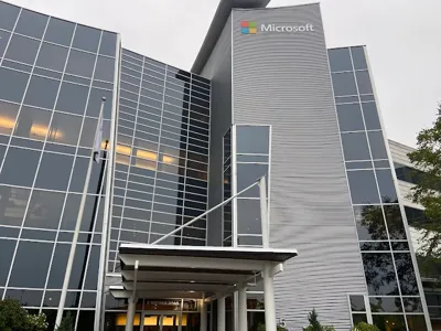 Modern corporate building with Microsoft branding featuring sleek glass and metallic facade, showcasing the company’s entrance with a covered walkway and adjacent landscaped area.
