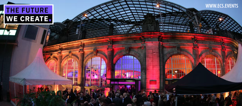 Elegant historic venue adorned with vibrant red lighting, hosting a bustling corporate or networking event. Large arched windows and a grand glass-roofed structure frame an engaged audience under white tents.
