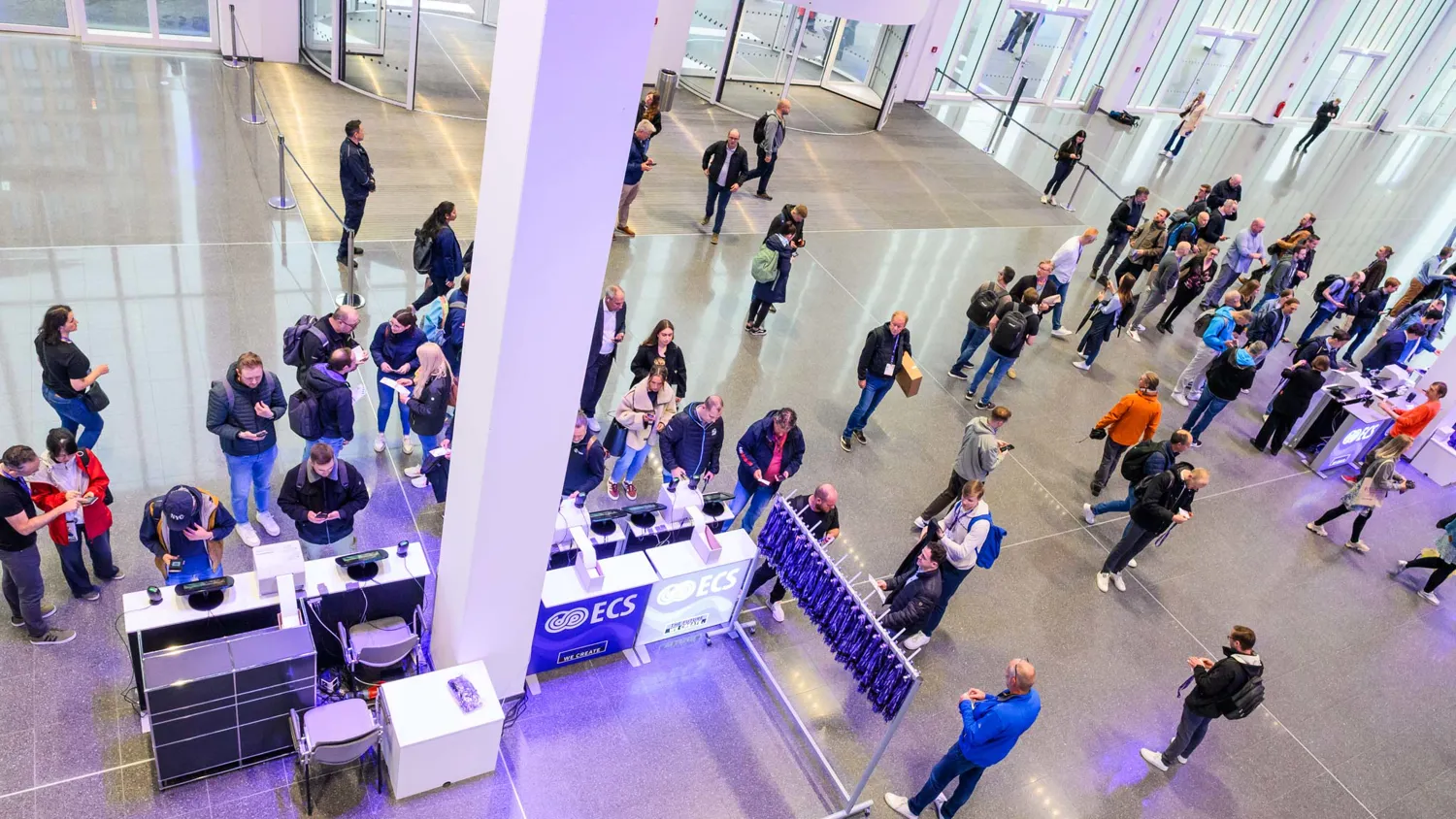 Attendees gather around booths in a modern convention hall, engaging with displays and each other. The scene captures professional networking and event activities in a spacious, well-lit indoor setting.