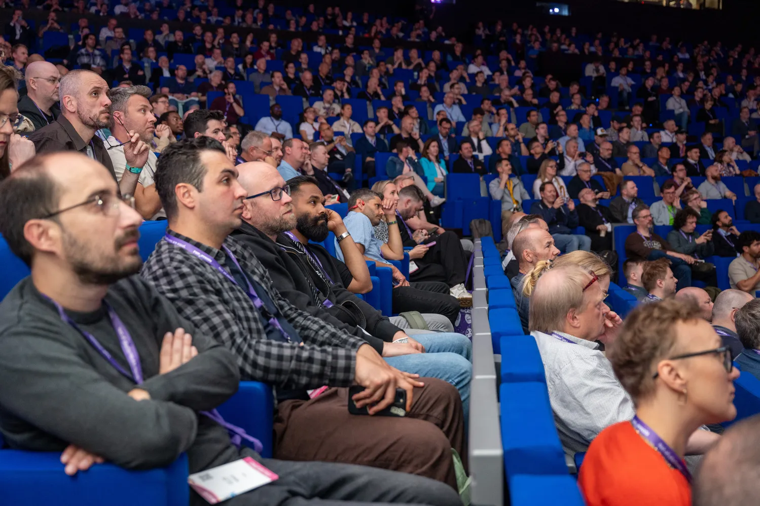 A large audience of professionals attends a conference or seminar in a spacious venue. Attendees are seated in rows, engaged and focused on the event proceedings.