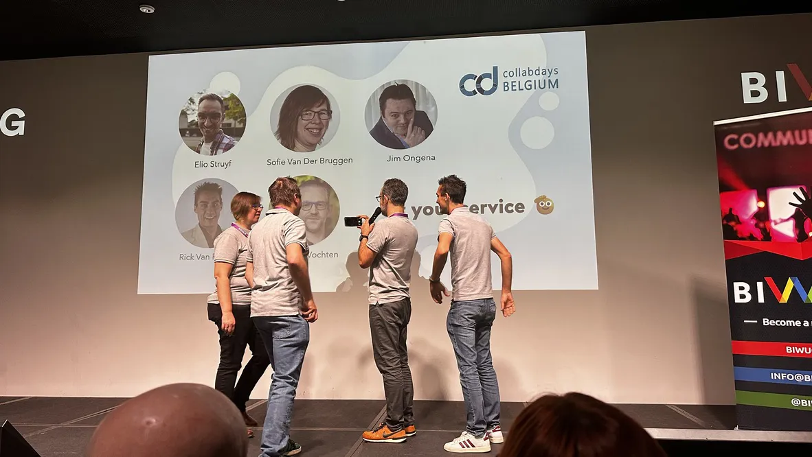 A group of individuals engages in a panel discussion or Q&A session at a professional event. The backdrop displays logos for CollabDays Belgium and BIWU, featuring participant photos and event branding.
