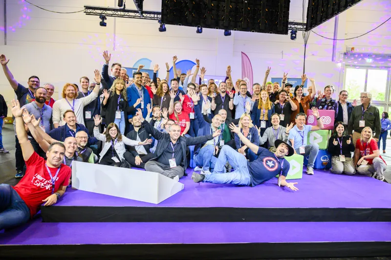 A group of attendees celebrating together on a purple stage at ECS