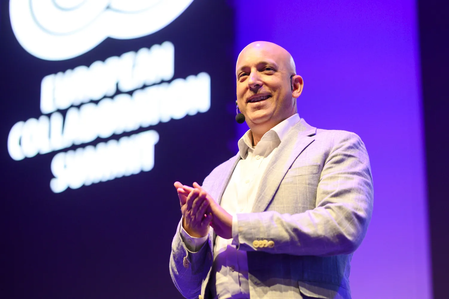 A conference speaker in a light jacket delivering a presentation with animated gestures