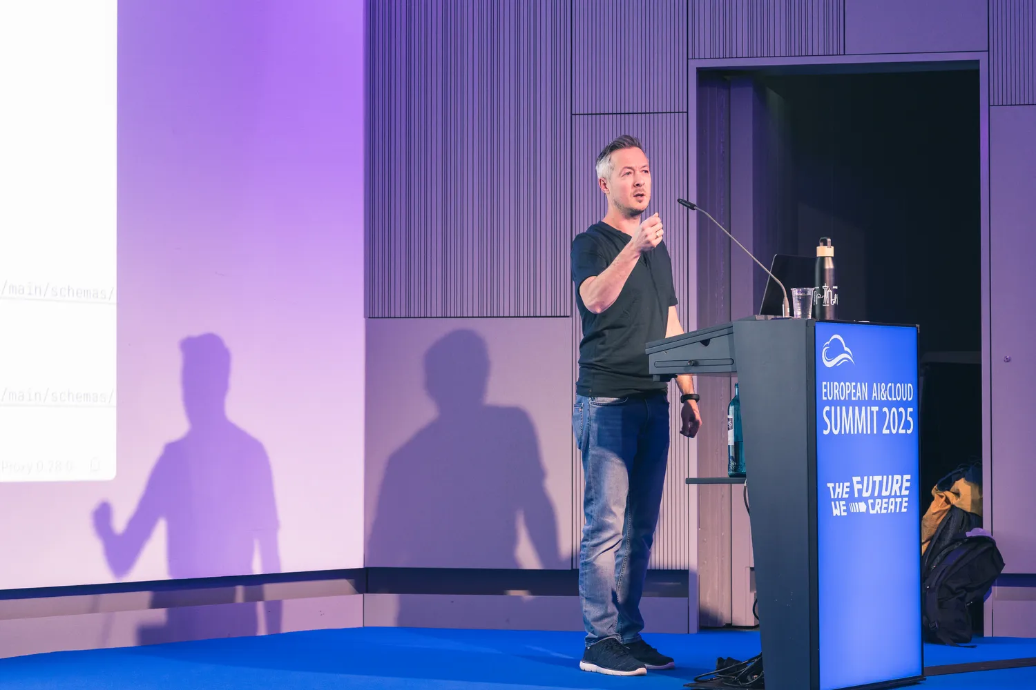 A speaker presenting from a conference podium to an audience at a technology summit.
