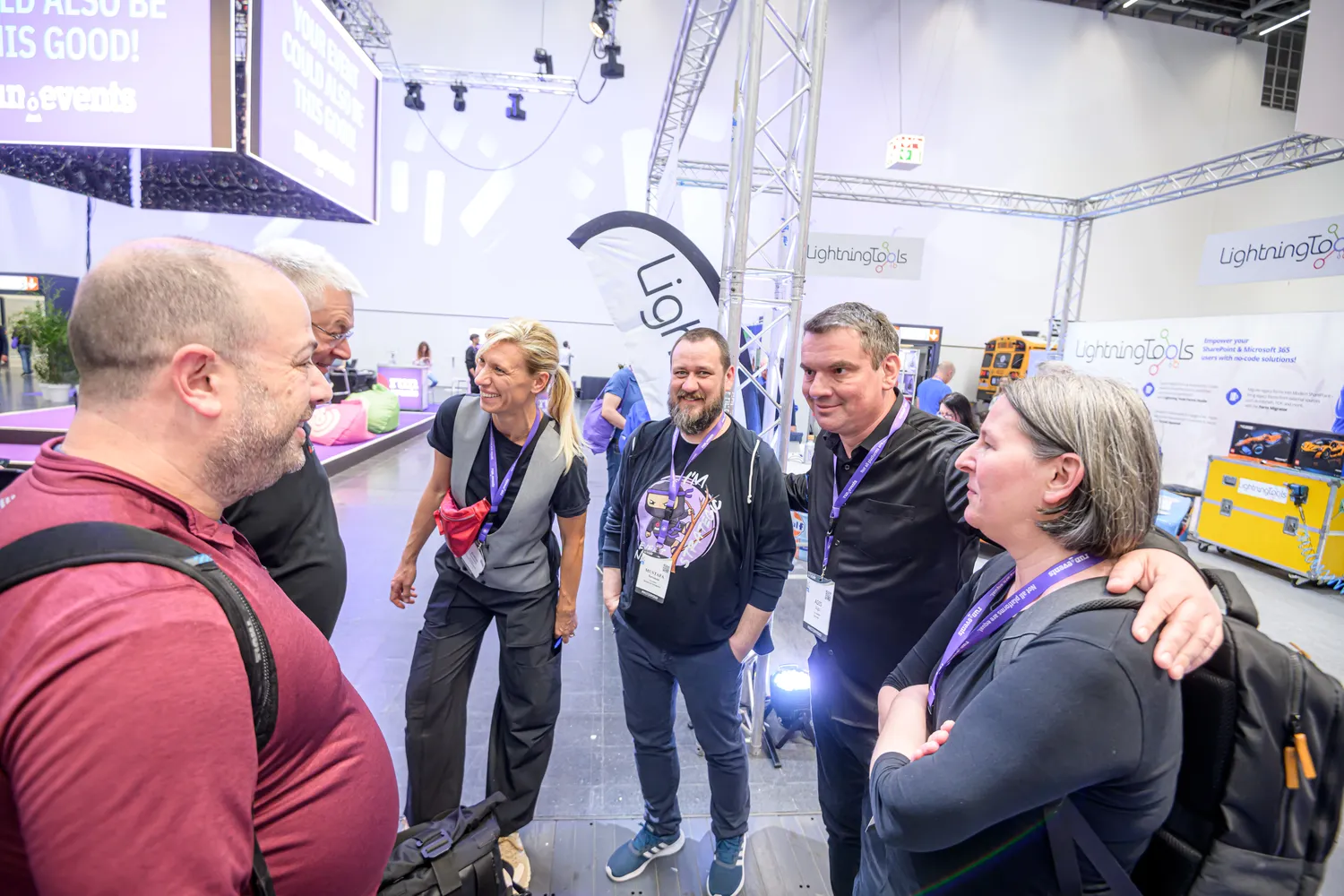 Professional attendees engaged in discussions at a tech trade show booth, featuring branded signage and interactive displays. The scene captures a lively exchange among individuals in business attire, set against an exhibition hall backdrop.