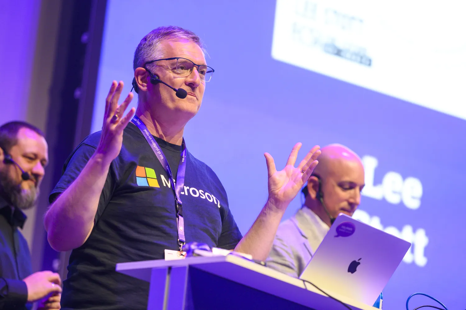 A speaker presenting energetically at a conference podium under stage lighting