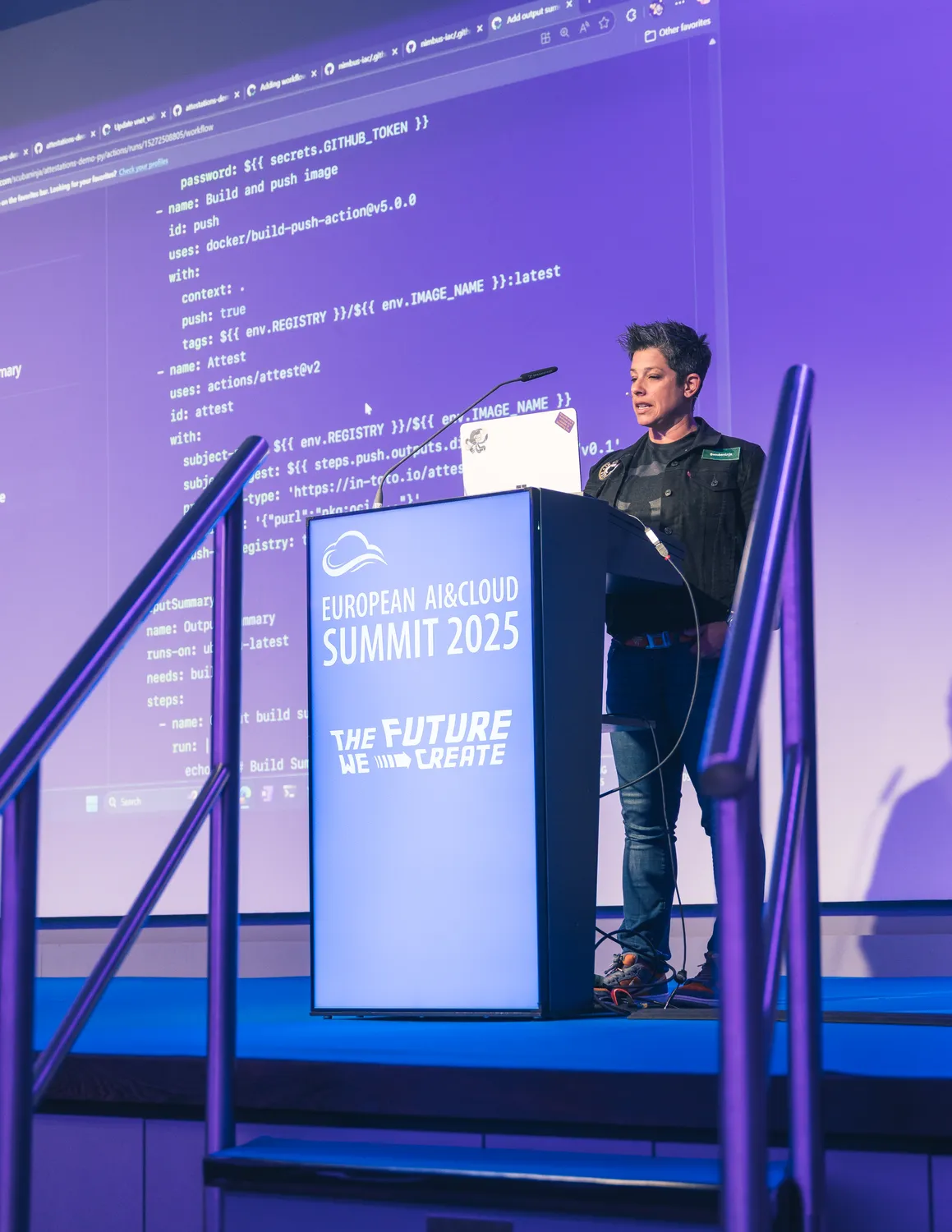 A speaker stands at a podium during the European AI & Cloud Summit 2025, delivering a presentation. The backdrop displays the event branding with the tagline "The Future We Create," alongside technical code snippets on a digital screen.