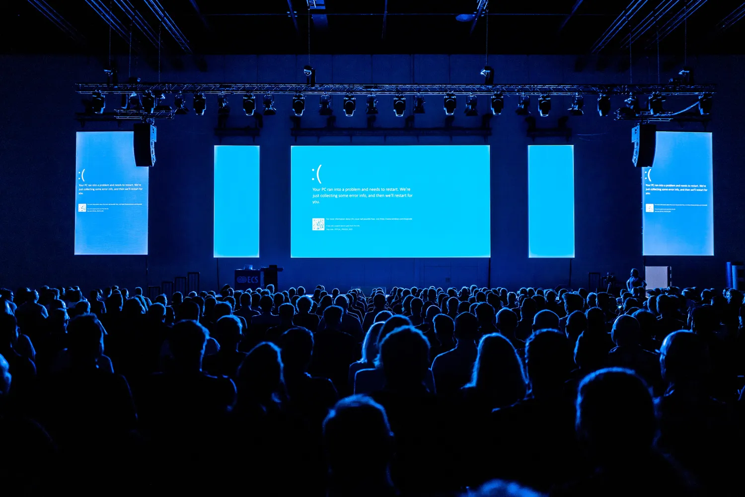 A large conference audience facing a stage with projected content on screen