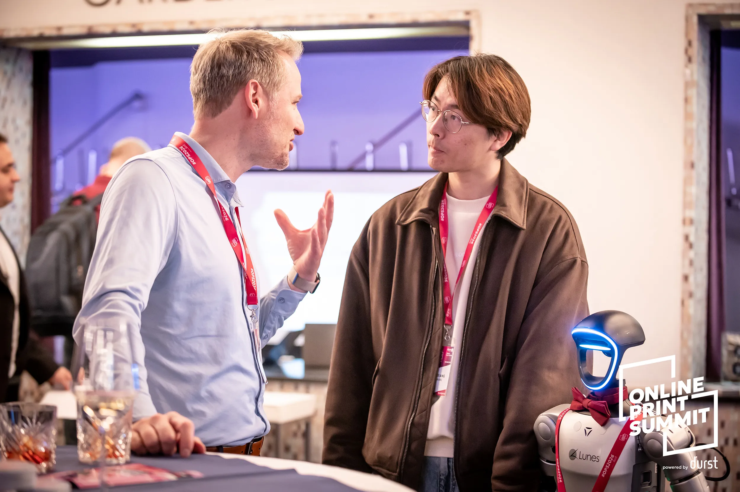 Zwei Teilnehmende im Gespräch an einem Partnerstand des Online Print Summit