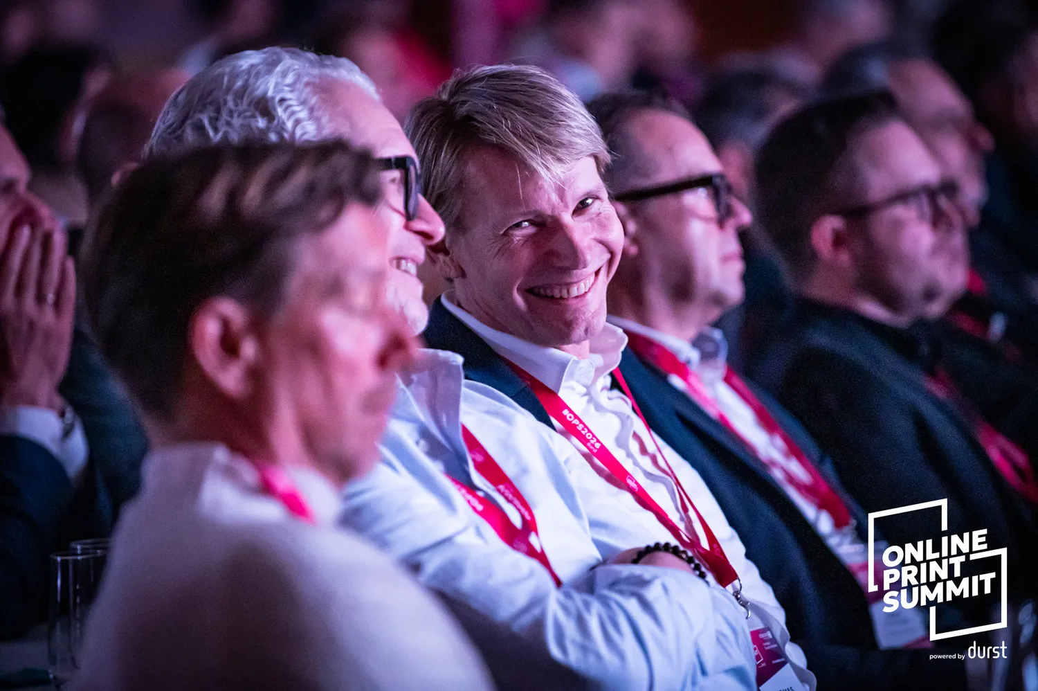 Professional attendees listen closely and take part in a summit session in a dimly lit conference setting.