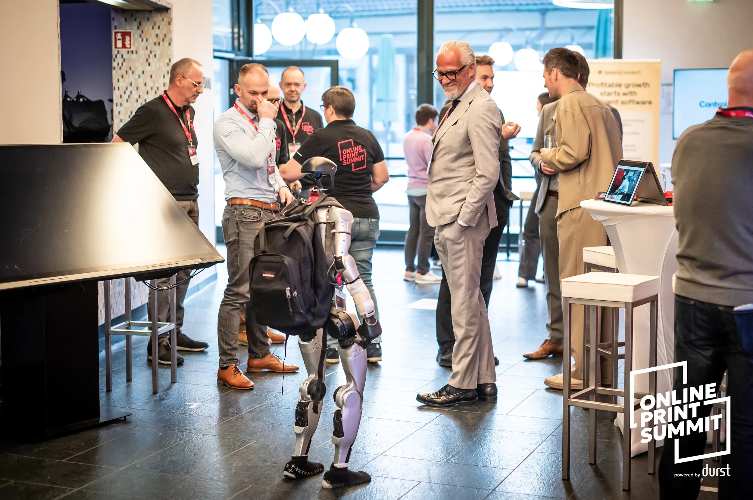 Summit attendees discuss technology beside a demonstration area in a modern conference venue.
