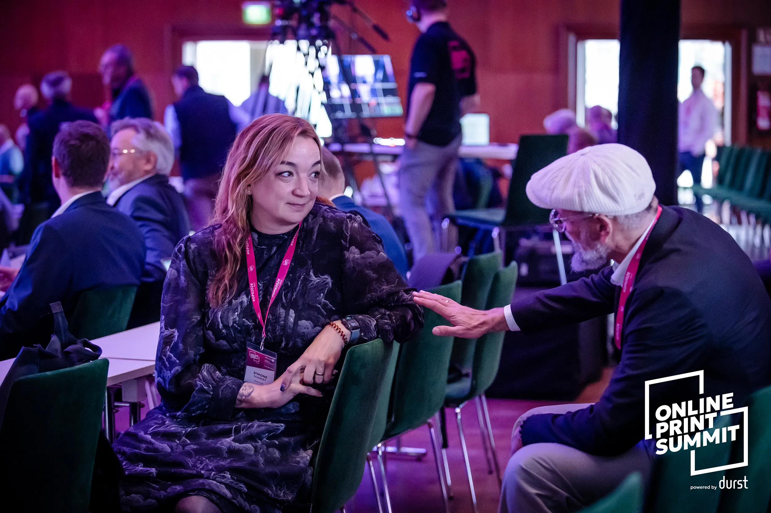 Attendees in business attire talk with each other during a professional summit networking break.