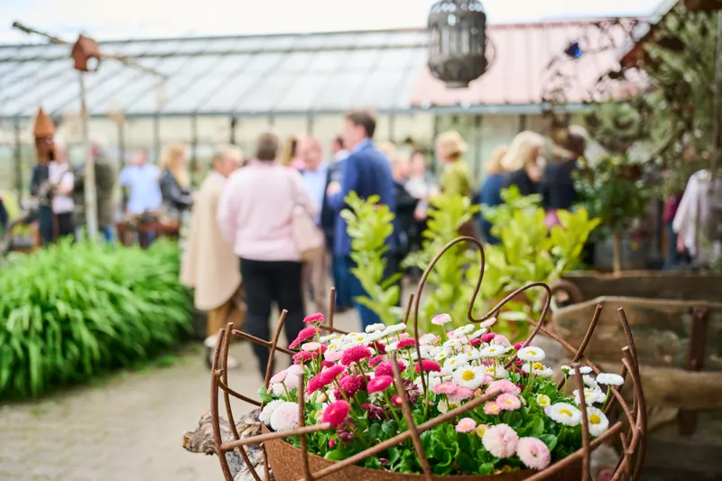 Menschen feiern gemeinsam im GenussGarten zwischen Gewächshaus und Garten.