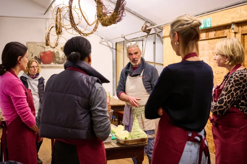 People cooking together around a table with fresh ingredients in a rustic kitchen setting