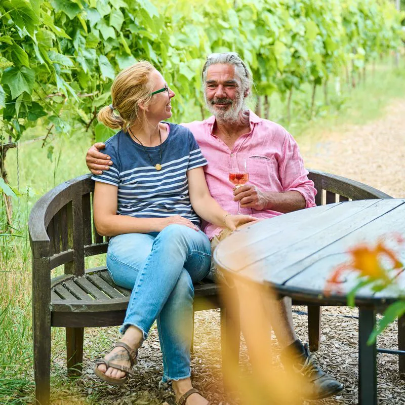 Maike und Steffen Bischof sitzen gemeinsam im GenussGarten und blicken entspannt in die Kamera.