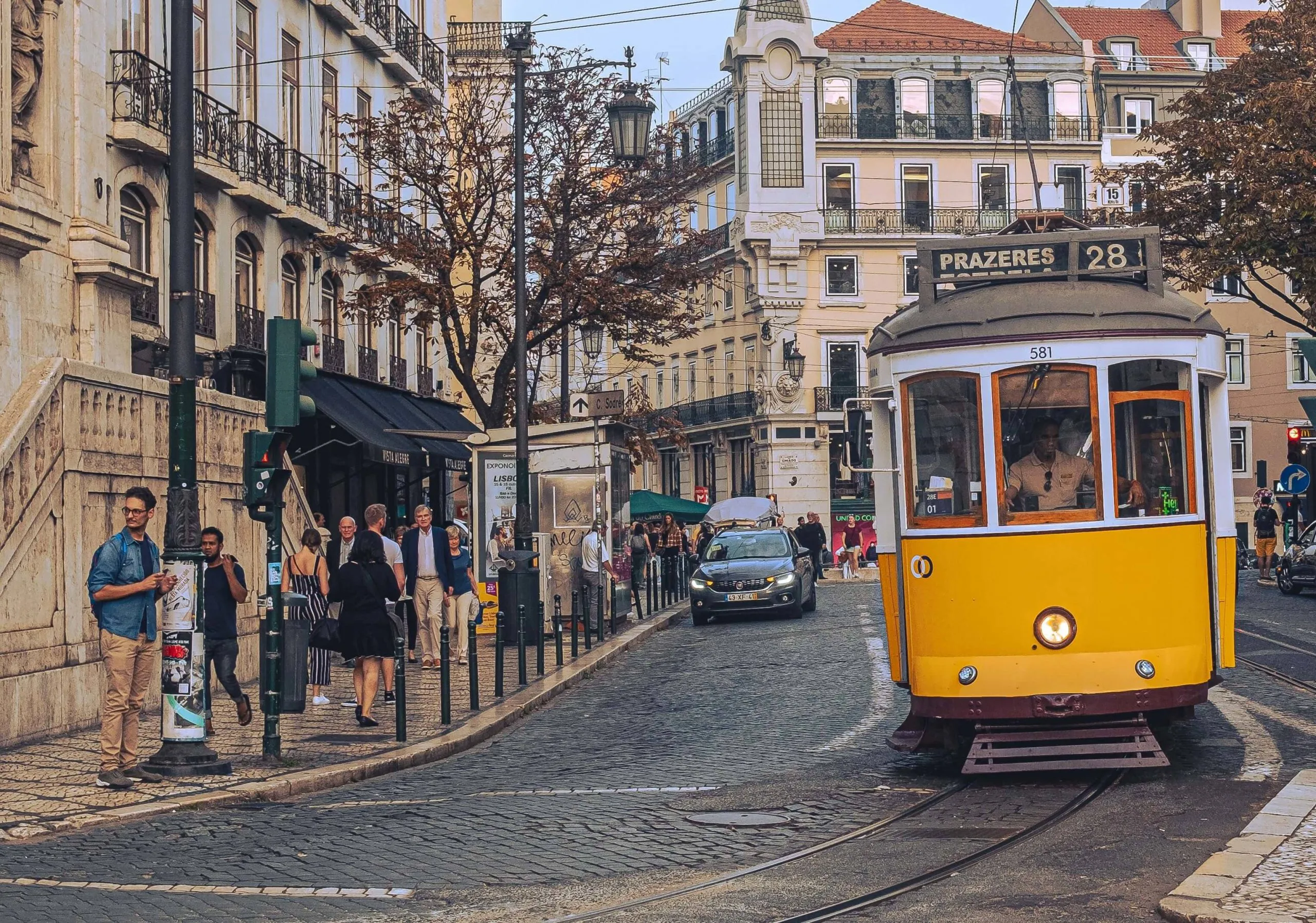 Historic Lisbon street with a yellow tram, cobblestones, cafes and people walking