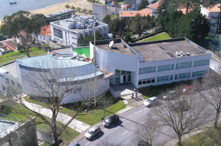 Aerial view of a contemporary event facility featuring a prominent circular building with a modern architectural design. The complex includes additional structures, landscaped greenery, and a paved area with parked vehicles.